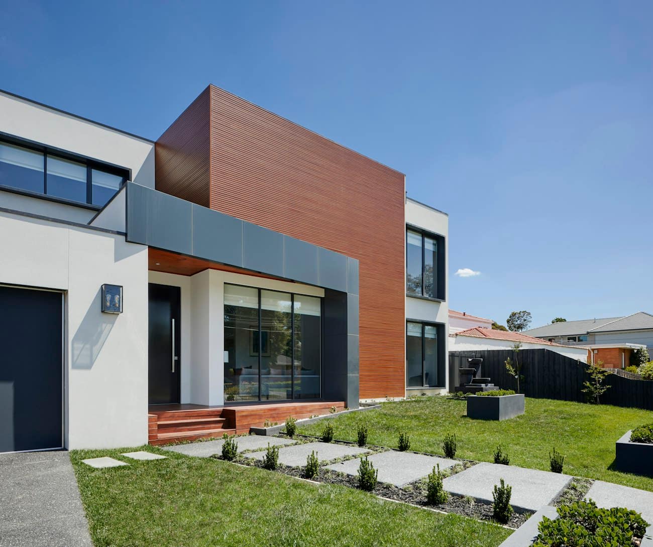 Ahşap ve gri panellerle giydirilmiş, peyzajlı bahçesiyle modern bir konutun girişi